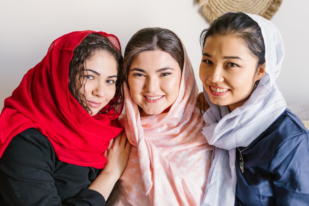 Three Iranian teenagers with head coverings smiling at the camera