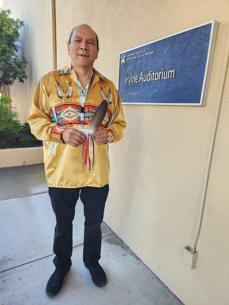 Native man in traditional shirt holding an eagle feather