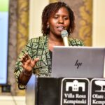 a woman standing behind a laptop speaking into a microphone